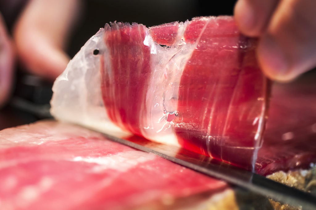 Close up of hand and knife cutting jamon iberico in Spain.